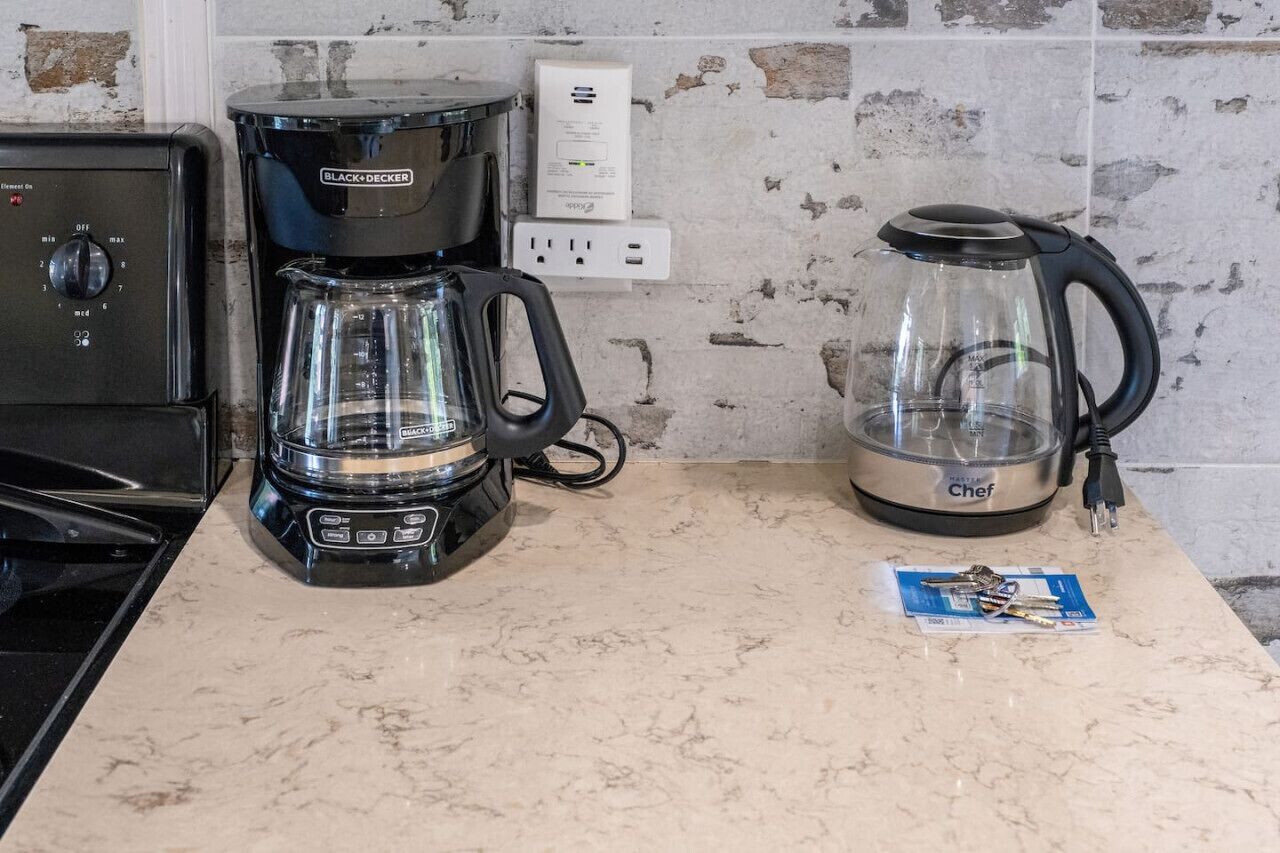A kitchen with a coffee maker, a kettle, and a stove.