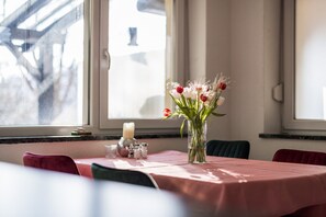 A dining table with a pink tablecloth, a vase of flowers, salt and pepper shakers, and a candle.