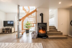 A modern living room with a wooden staircase, a fireplace, a television, and a plant. - Apartment in Hötting near Nordkette (Innsbruck)