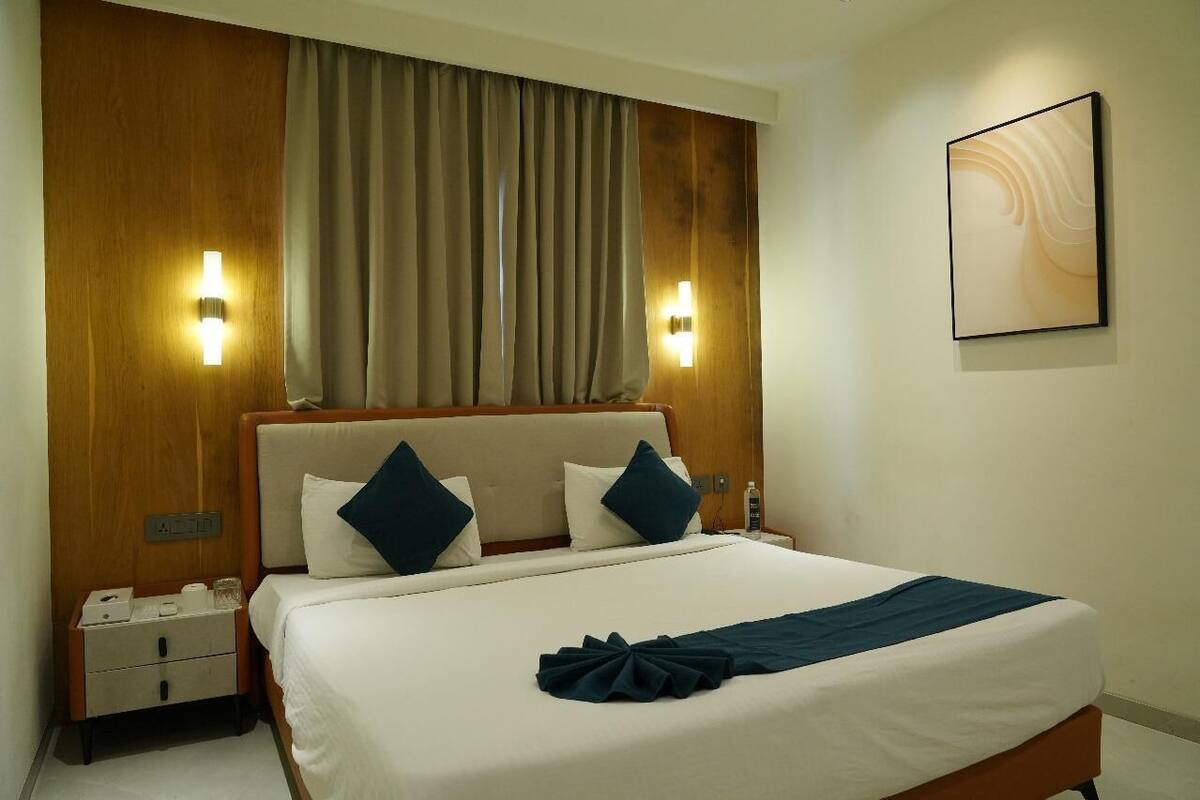 Habitación de hotel con una cama grande, dos lámparas de noche, cabecera de madera, una cortina y una obra de arte colgada en la pared.