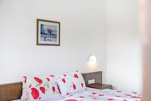 A bed with floral bedding, a bedside table, a wall-mounted light, and a framed picture on the wall.