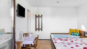 Habitación de hotel con cama, escritorio, silla, televisor y lámpara de pared.