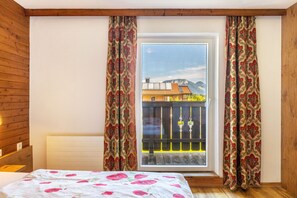 Une chambre avec une grande fenêtre, des murs en bois, un lit recouvert d’une courtepointe à motifs floraux et des rideaux à motifs floraux.