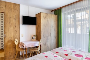 Een slaapkamer met een bed, een houten garderobe, een bureau met stoel en een televisie aan de muur.