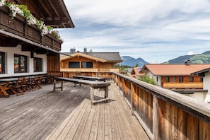 Een houten terras met banken en tafels, met uitzicht op een bergachtig landschap.