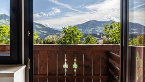 A balcony with a wooden railing, a view of mountains, and a clear sky.