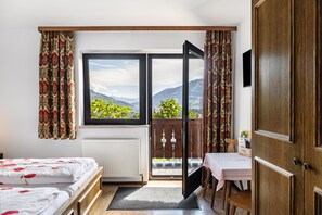 Une chambre à coucher comprenant un lit, un bureau, une chaise, un radiateur, une fenêtre donnant sur les montagnes et une porte.