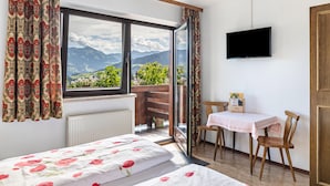 A bedroom with a large window, a bed, a table with a chair, and a TV.