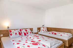 Dos camas individuales con cabeceros de madera, ropa de cama blanca con motivos florales rojos y una lámpara de pared.