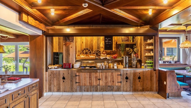 Ein Barbereich aus Holz mit rustikalem Design, mit einer Kreidetafel-Speisekarte, Holzschränken und Blick ins Freie.