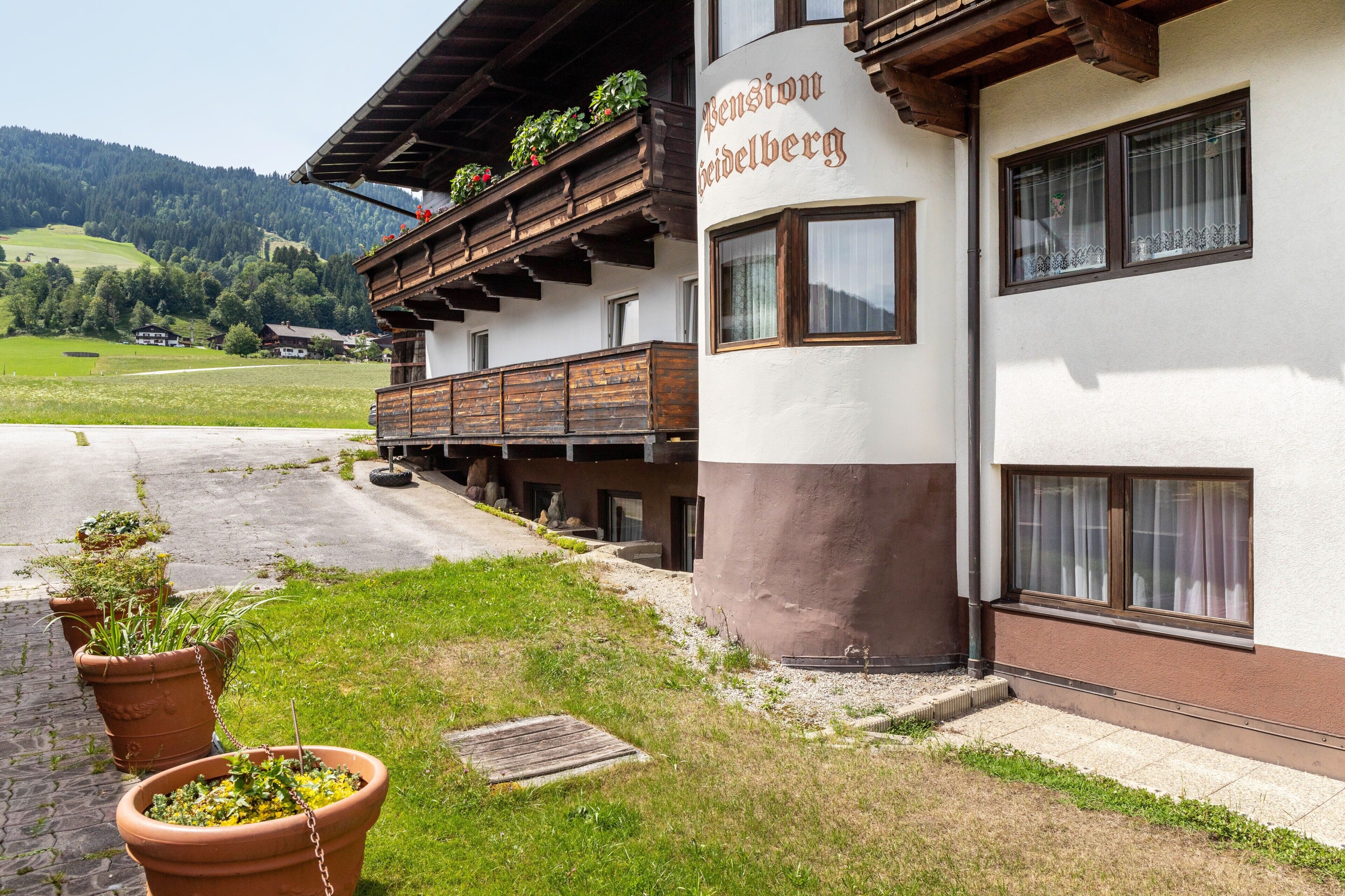 Ein Gebäude mit Balkon, einem Schild mit der Aufschrift 'Pension Gaisberg' und Blick auf eine grüne Landschaft.