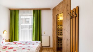Ein Schlafzimmer mit einem Bett, grünen Vorhängen, einem Holzschrank und einem Badezimmer mit einem Waschbecken.