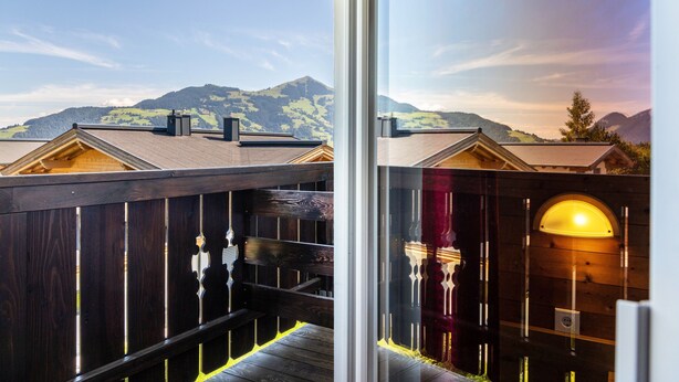 Una terraza de madera con barandilla de cristal con vistas a un paisaje montañoso.