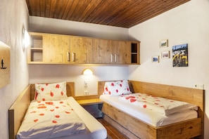 A room with two wooden beds, a wooden cabinet, a wall-mounted light, and framed pictures. - Room 'Familienzimmer 10' with Mountain View, Shared Terrace and Wi-Fi (Hopfgarten im Brixental)