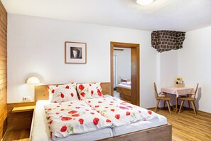 A bedroom with a wooden bed, a bedside table, a chair, a small table with a box, and a mirror.