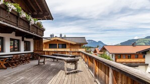 A wooden deck with outdoor seating, a view of mountains, and traditional chalet-style buildings. - Room '06' with Mountain View, Shared Terrace and Wi-Fi (Hopfgarten im Brixental)