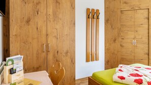 A bedroom with wooden wardrobes, a bed with a green mattress, and a wall-mounted ski rack. - Room '16' with Mountain View, Shared Terrace and Wi-Fi (Hopfgarten im Brixental)