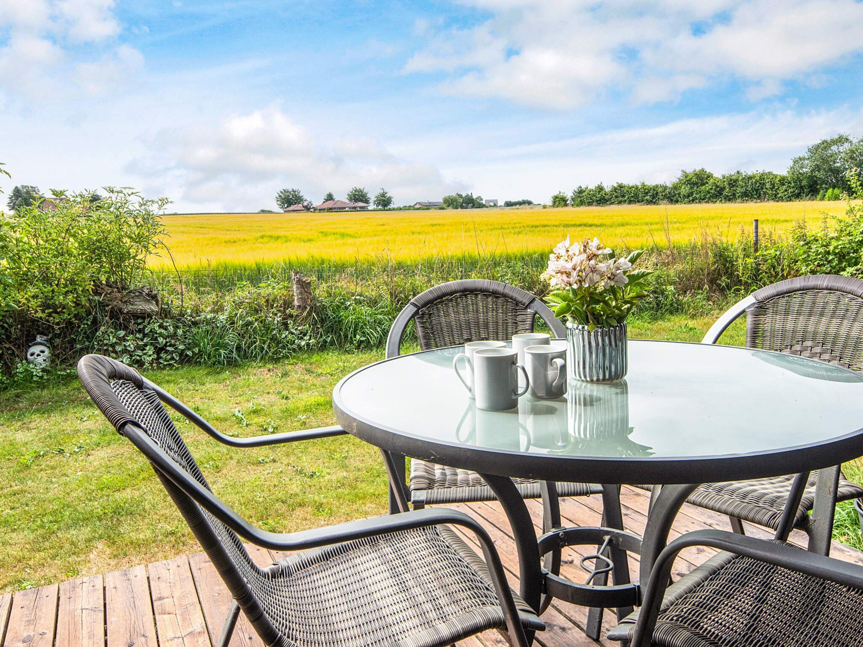 An outdoor dining area with a round table, four chairs, and a vase with flowers.