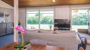 Un salon avec un plafond en bois, un canapé gris, un téléviseur et une table sur laquelle est posée une plante en pot.