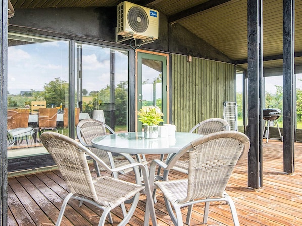 An outdoor dining area with wicker chairs and a glass table, overlooking a garden. - 6 Person Holiday Home in Juelsminde (Horsens)
