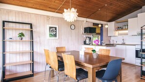 Un coin repas avec une table et des chaises en bois, un luminaire suspendu et une cuisine en arrière-plan.