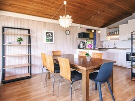 Un comedor con una mesa y sillas de madera, una lámpara colgante y una cocina al fondo.