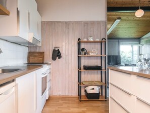 A kitchen with white cabinets, a wooden countertop, a black oven, and a wooden shelf with kitchen items. - 6 Person Holiday Home in Juelsminde (Horsens)