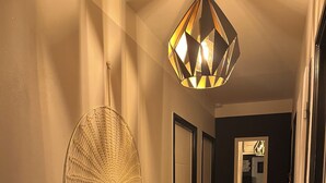 Ein Flur mit Wandbehängen aus Makramee, einer geometrischen Pendelleuchte und einem Spiegel an der Wand.