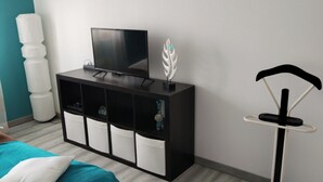 Ein Schlafzimmer mit einem Bett, einem Fernseher auf einem schwarzen Schrank, einem weißen, flauschigen Teppich und einem weißen Dekoelement auf dem Schrank.