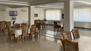 A spacious dining area with multiple tables and chairs, a flat-screen TV mounted on the wall, and large windows with blinds. - Arena Hotel Goychay (Goychay)