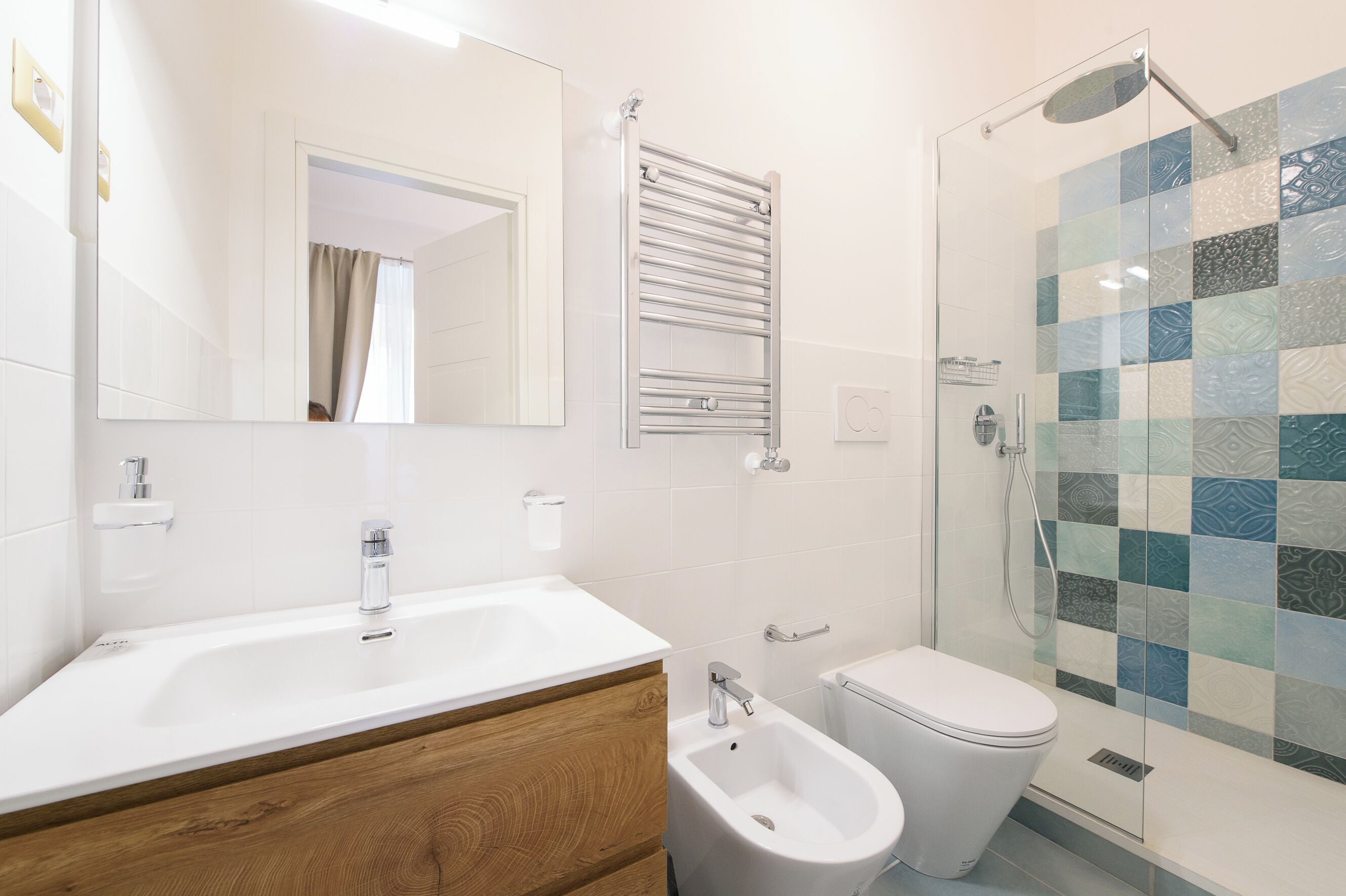 A modern bathroom with a white sink, bidet, toilet, and a glass shower enclosure.