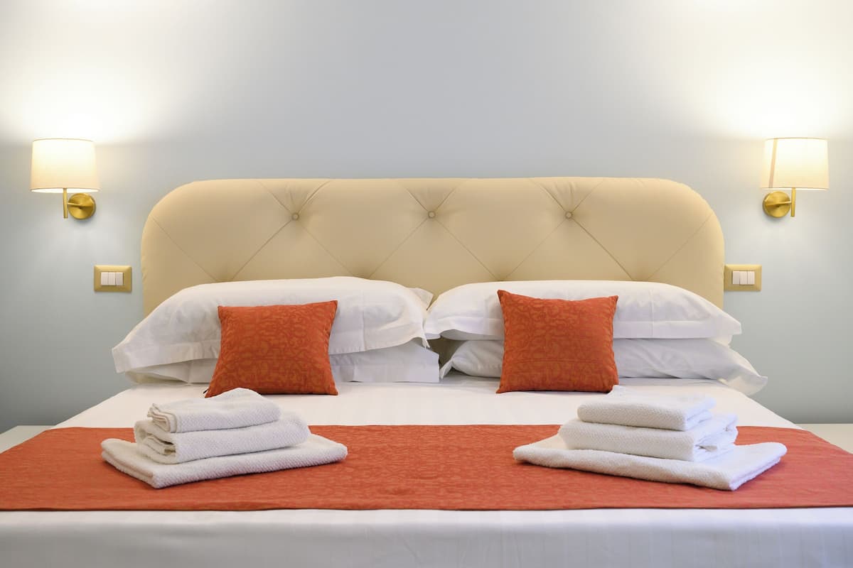A hotel room with a bed, two pillows, two wall lamps, and a red blanket.