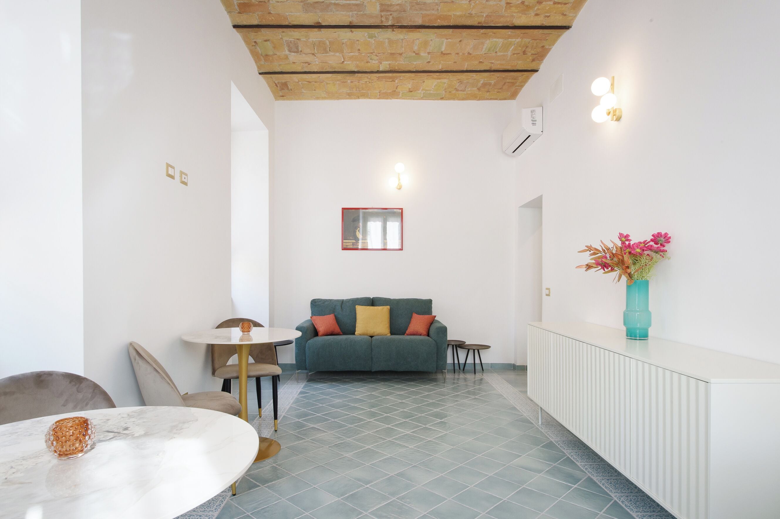 Un saló modern amb un sofà verd, una taula de console blanca amb un vas, i una zona de menjador amb una taula de marbre.
