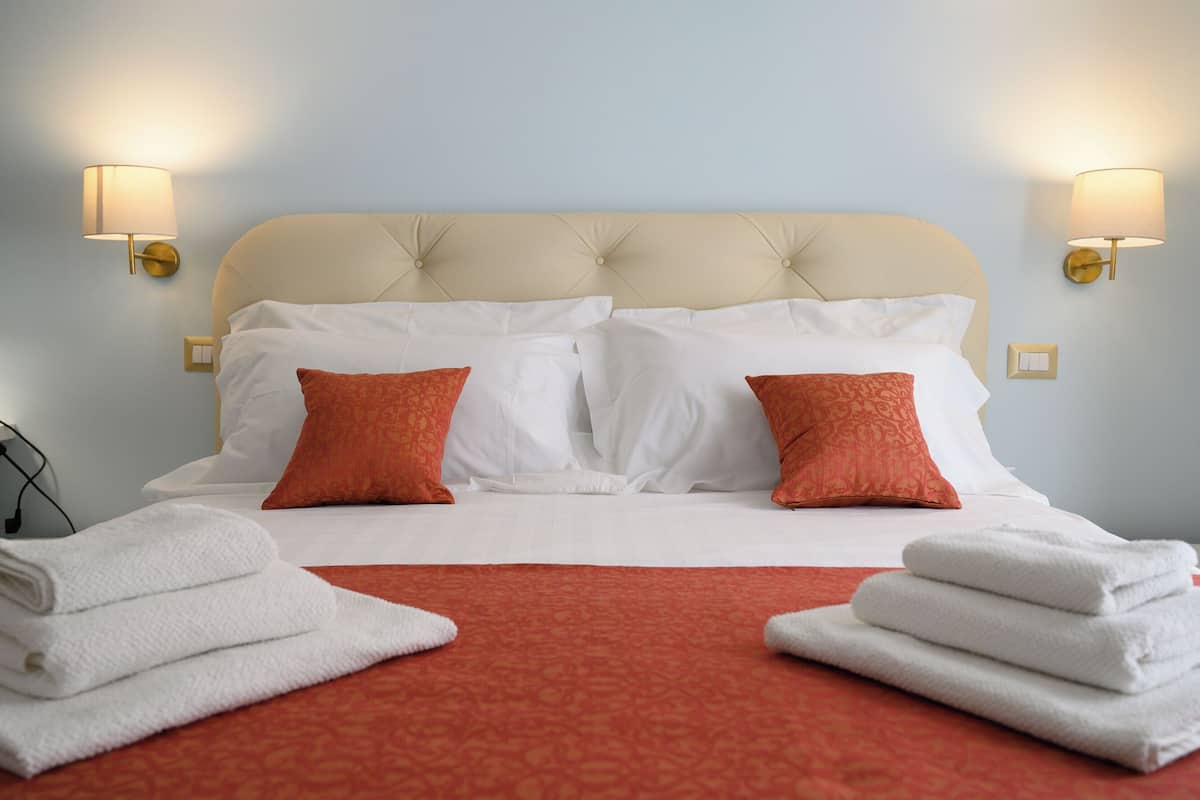 A neatly made bed with white and red pillows, a red bedspread, and two wall-mounted lamps.