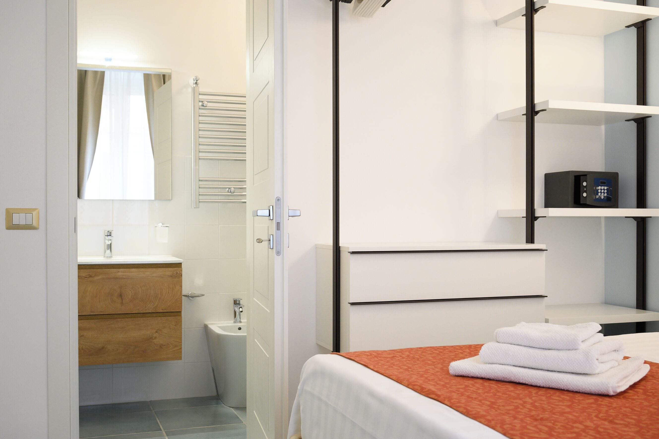 Habitació d'hotel amb bany, un llit amb estriatge taronja i una petita estant amb un objecte negre.