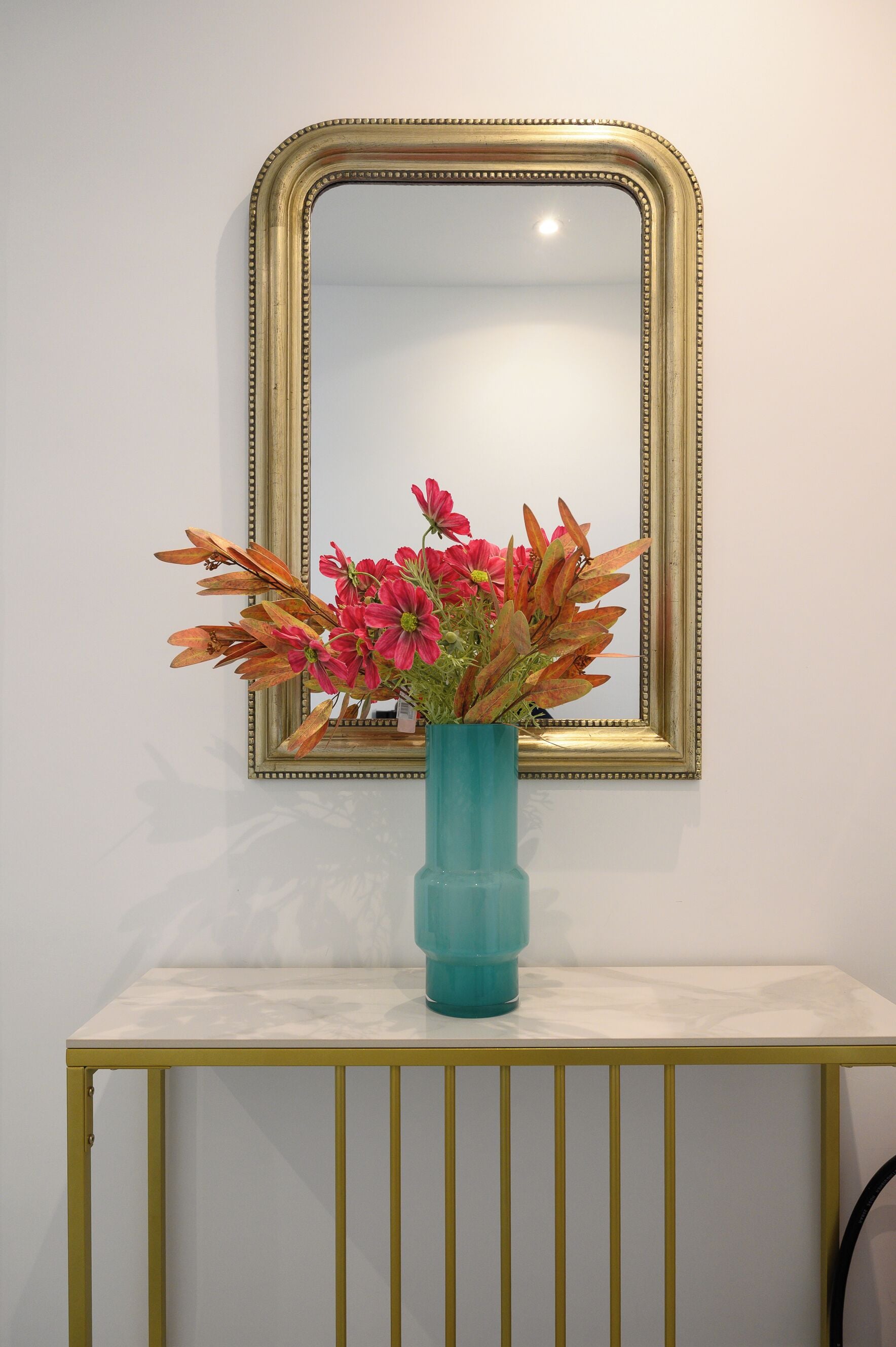 A teal vase with pink flowers on a white marble console table.