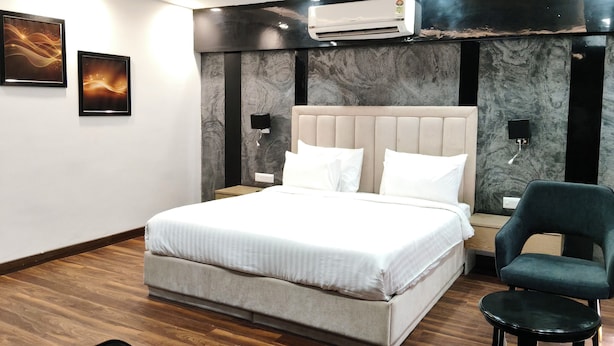 A modern bedroom with a large bed, a ceiling fan, an air conditioning unit, and a dark green chair. - Clarks Inn Express Firozabad (Firozabad)