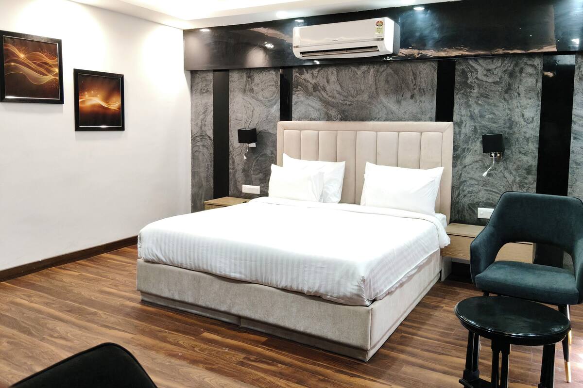 Um quarto moderno com uma cama grande, um ventilador de teto, um aparelho de ar condicionado e uma cadeira verde escura.