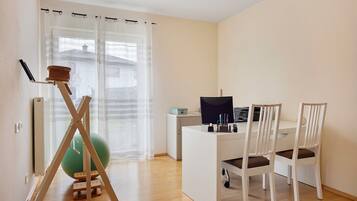 Ein Zimmer mit Schreibtisch, zwei Stühlen, einem Computer, einem grünen Gymnastikball und einem Stehtisch mit Sitzmöglichkeit.