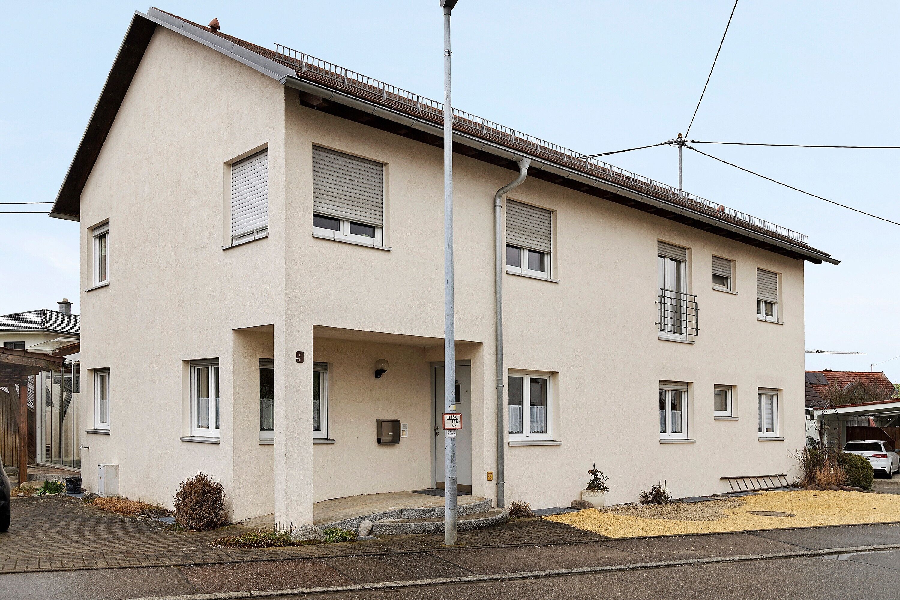 Ein zweistöckiges Gebäude mit Flachdach, einem Balkon im zweiten Stock und einer kleinen Veranda.