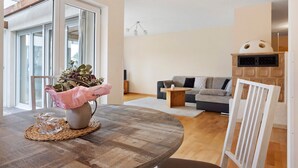 Una sala de estar con una mesa redonda de madera, un sofá, una silla blanca y una chimenea de piedra.
