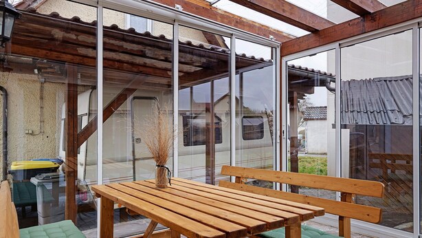 Mesa y banco de madera en un porche cubierto con puertas de vidrio.