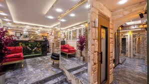 A lobby with stone walls, a reception desk, and red sofas. - REN PLUS SUİTES OTEL (İstanbul)