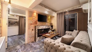 A modern living room with a stone fireplace, a flat-screen TV mounted above it, and a plush sectional sofa. - REN PLUS SUİTES OTEL (İstanbul)