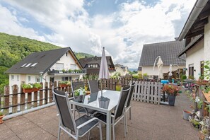 Une terrasse avec une table et des chaises, entourée d’une clôture en bois, avec des maisons et de la verdure en arrière-plan.
