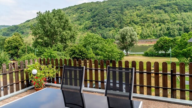 A table with chairs, a wooden fence, and a view of a green landscape with hills. - Apartment 'Moselglück' with Mountain View, Wi-Fi and Air Conditioning (Sankt Aldegund)
