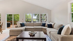 A spacious living room with a large sectional sofa, a wooden coffee table, and a view of the outdoors through large windows.