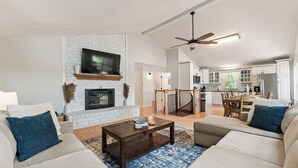 A spacious living room with a fireplace, a dining area, and a kitchen in the background.