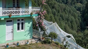 A green building with a balcony, surrounded by a mountainous landscape.