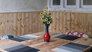A room with a wooden table, a vase with flowers, and a window with blinds.